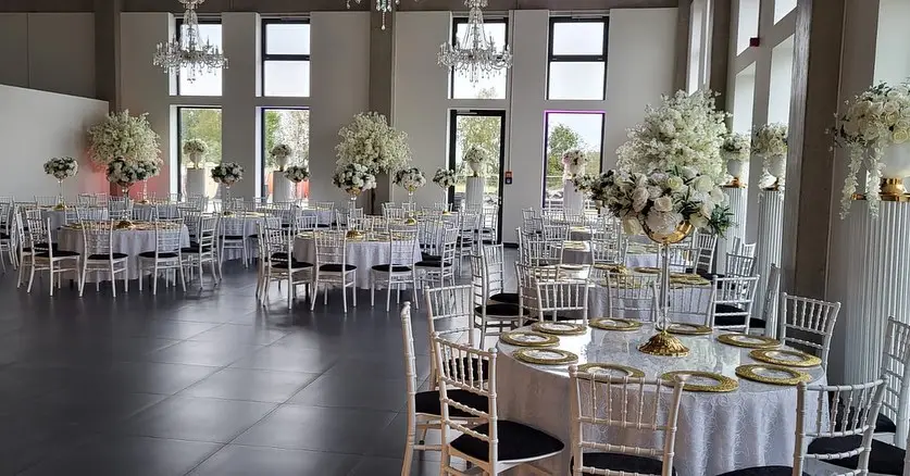 Saal mit hohen weißen Blumengestecken auf runden Tischen